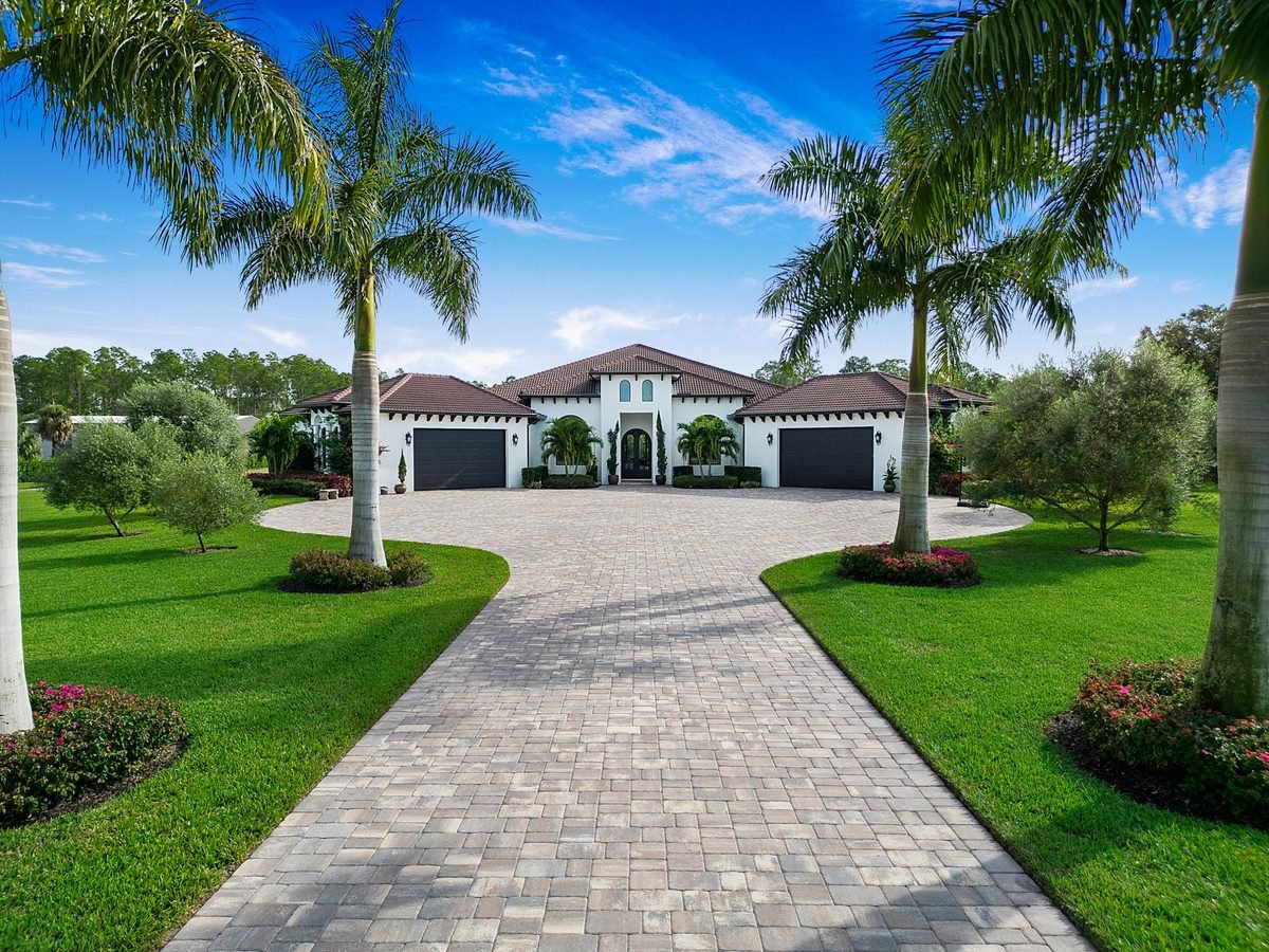 Luxury Naples home with circular paver driveway framed by twin royal palm trees