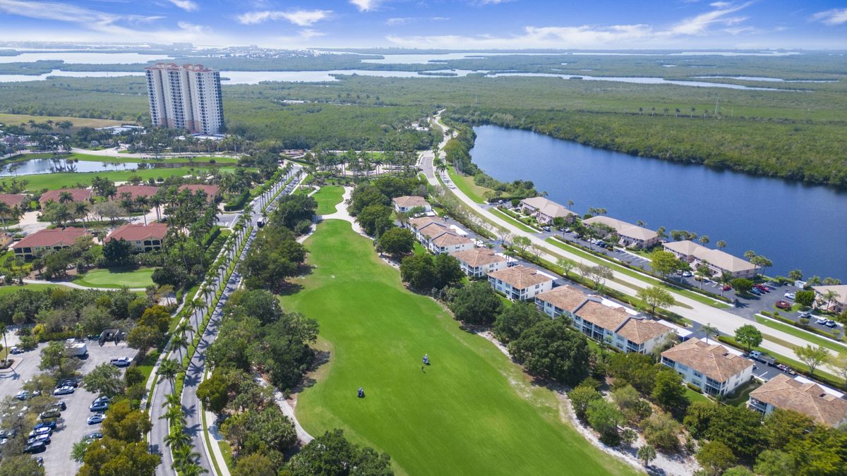 Aerial view of a Naples golf community with condos and a high-rise tower near the bay