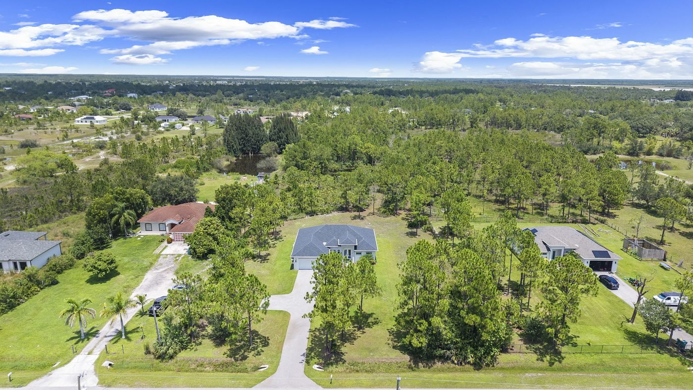 Wide aerial of Golden Gate Estates acreage lots with a new construction home, pine flatwoods and a pond in Naples, Florida