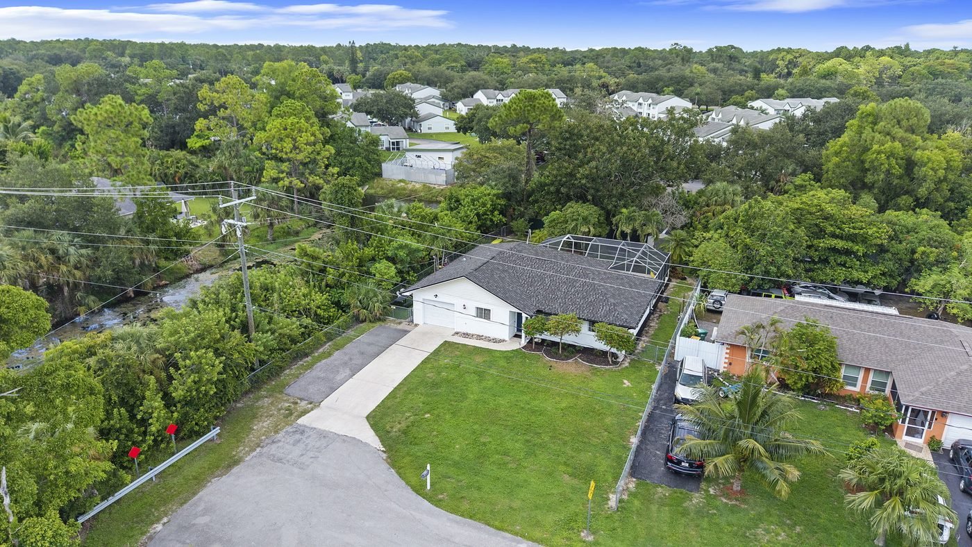 Aerial of a no-HOA Golden Gate City home with a wide driveway beside a freshwater canal in Naples, Florida