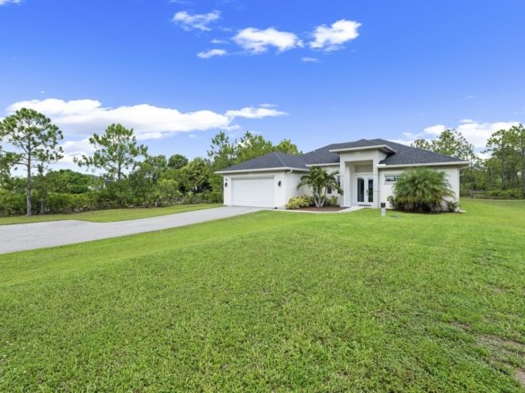 White 2021 single-story home on a wide green lawn under blue sky in Golden Gate Estates, Naples, Florida