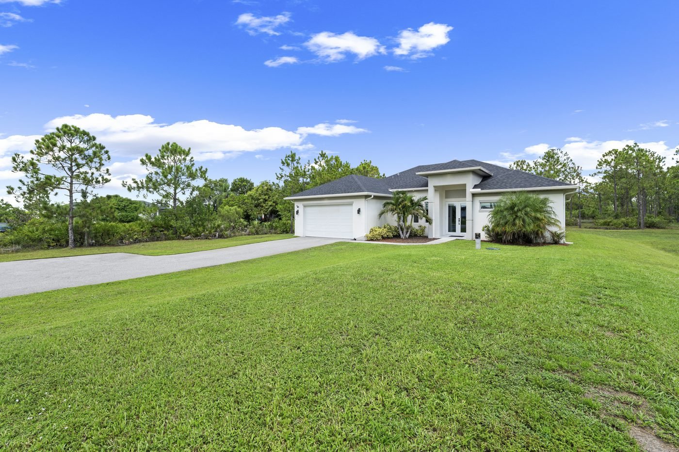 White 2021 single-story home on a wide green lawn under blue sky in Golden Gate Estates, Naples, Florida