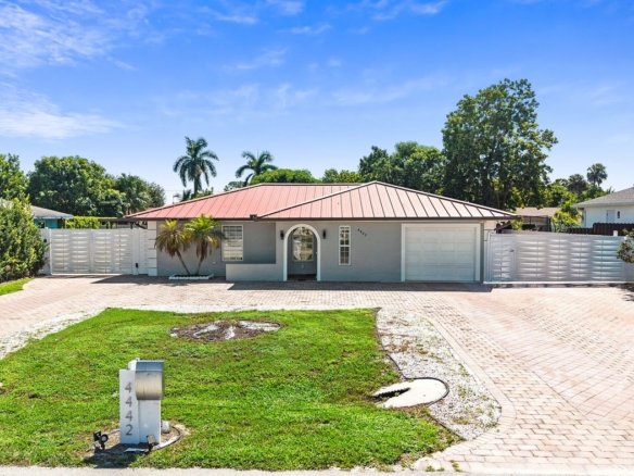 Front of a remodeled pool home with a metal roof and paver driveway in Golden Gate City, Naples, Florida