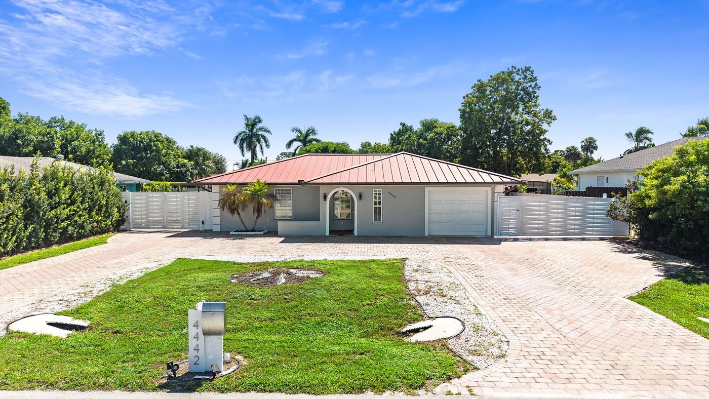 Front of a remodeled pool home with a metal roof and paver driveway in Golden Gate City, Naples, Florida