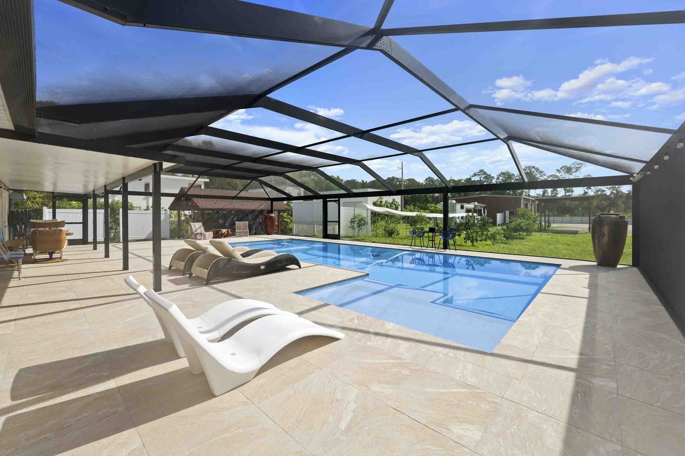 Screened pool with lounge chairs on a wide paver deck at a Golden Gate Estates home in Naples, Florida